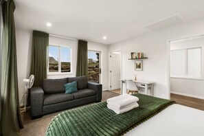 Ein Schlafzimmer mit Bett, Sofa, Schreibtisch und Blick ins Freie.