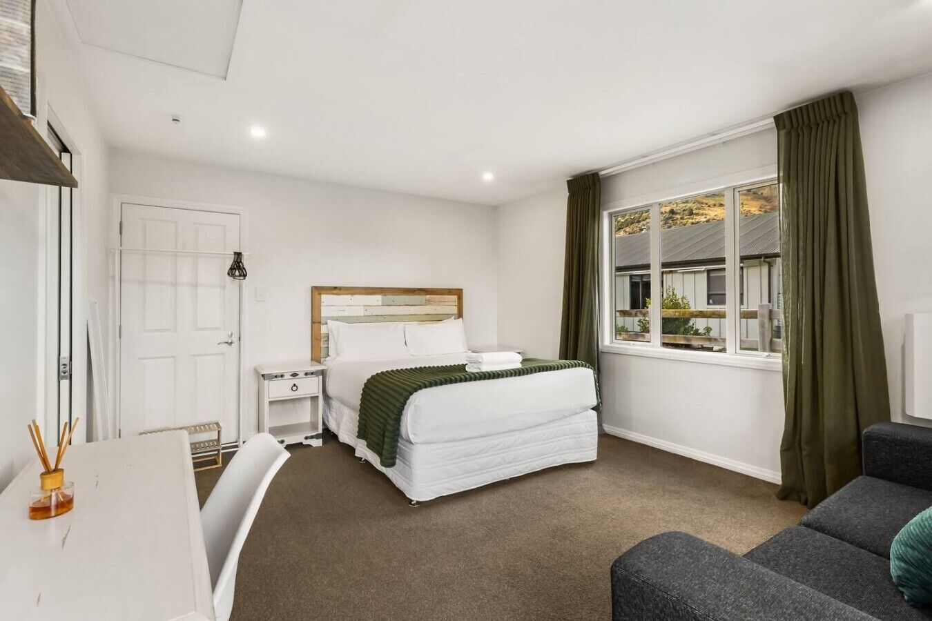 Cosy queen bedroom with mountain views, crisp white linens, and elegant dark curtains for a restful night`s sleep.