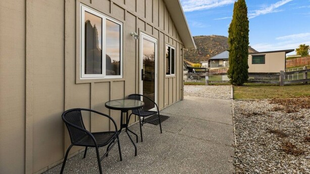 Un edificio con un patio attrezzato con due tavoli e quattro sedie, una porta e vista su una collina alberata.