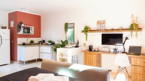 A modern living room with a sofa, a TV, a desk with a laptop, and a kitchen area with a microwave. - Charmoso na Vila Madalena com AC  (São Paulo)