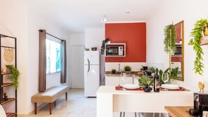 A modern kitchen with a built-in microwave, a dining area with a bench, and a small bar area with stools. - Charmoso na Vila Madalena com AC  (São Paulo)