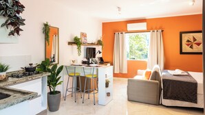 A modern kitchen with a gas stove, bar stools, and a dining table. There is a living area with a sofa and a bed. - Charmoso na Vila Madalena com AC  (São Paulo)