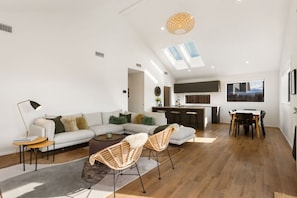 Ein moderner Wohnraum mit Sofa, Sesseln, einem Esstisch und einer Küchenzeile.