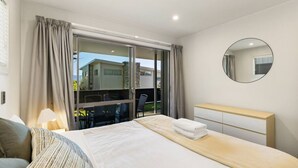 A modern hotel room with a large bed, a bedside table, a round mirror, and a view of the outside. - Lake & Alps on Your Doorstep | Resort Facilities (Wānaka)