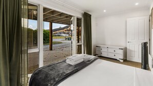 Ein Schlafzimmer mit Bett, Kommode, Fernseher und einer Glastür, die auf eine Straße und Gebäude mit Blick blickt.