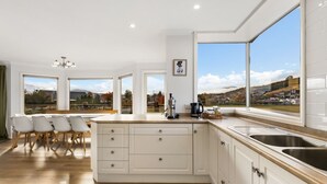 Eine moderne Küche mit einer großen Kochinsel, weißen Schränken und Blick auf eine Stadt durch große Fenster.