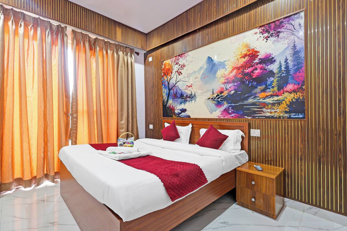 A hotel room with a large bed, wooden paneling, a nightstand, and a painting of a landscape.