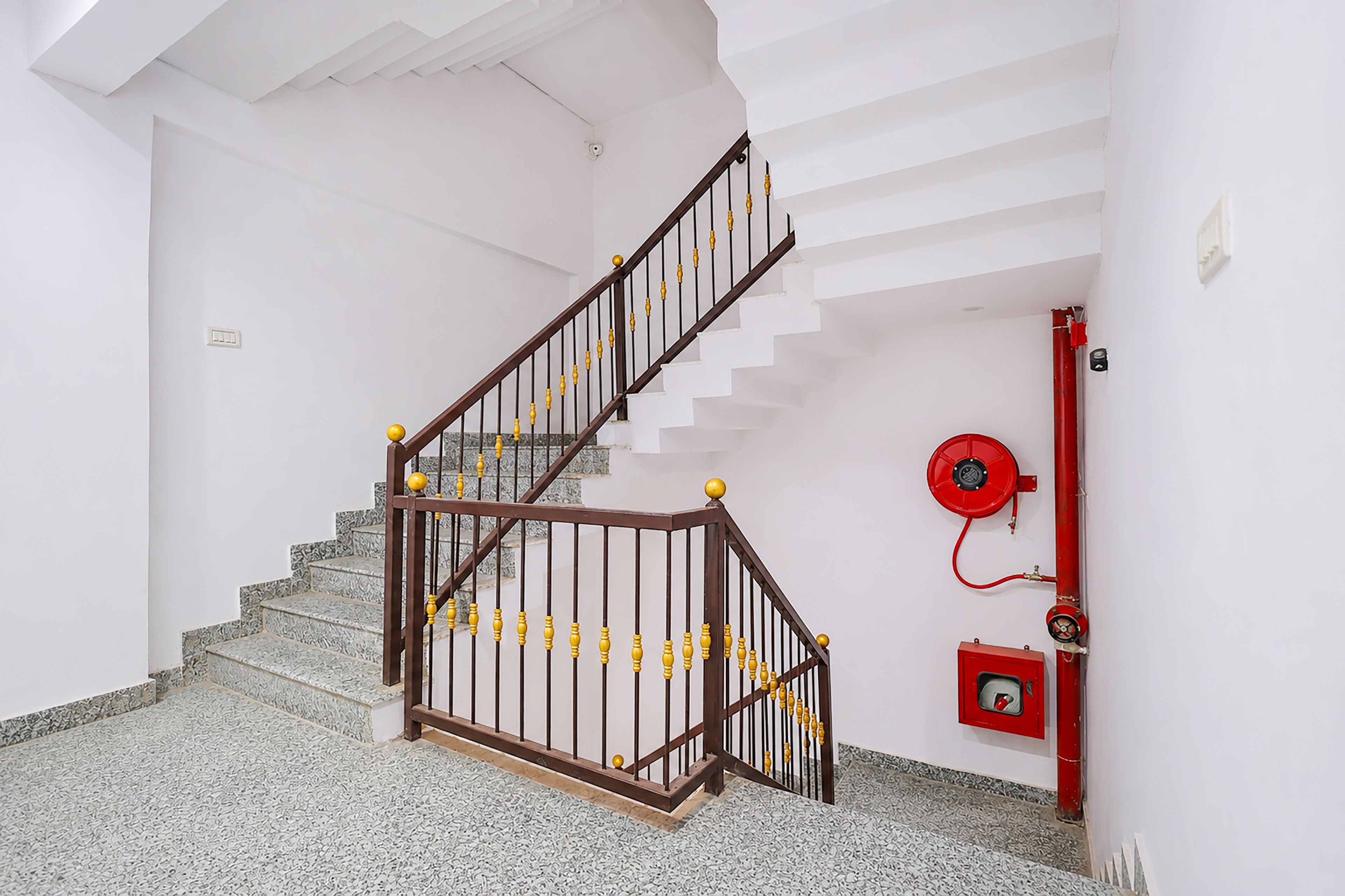 A staircase with a wooden handrail and metal balusters, a red fire hose reel, and a fire alarm box on the wall.