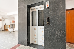 An elevator with a control panel, a reception desk, and a wooden door with the number 002. - Hotel Rahi Residency (Varanasi)