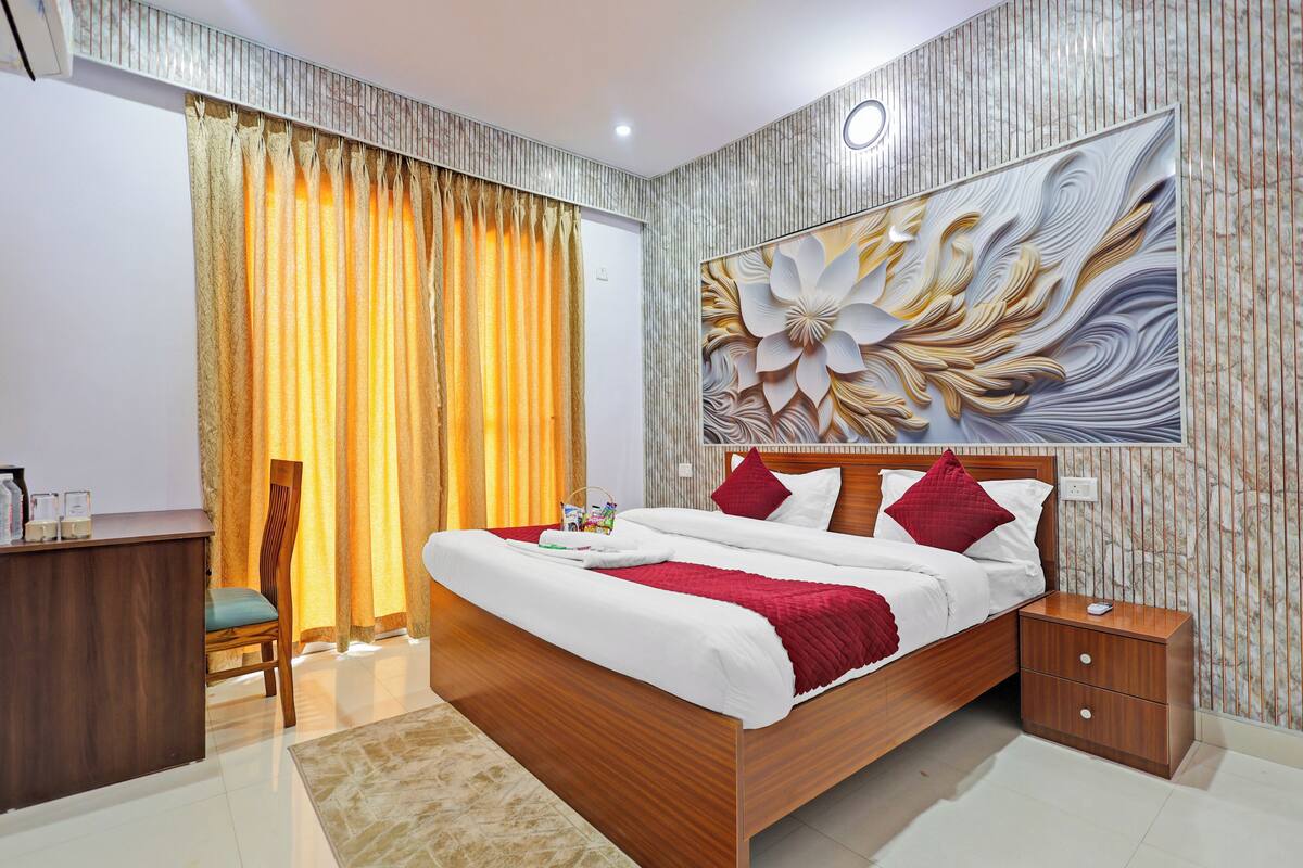 A bedroom with a bed, nightstand, desk, chair, and a large floral artwork on the wall.