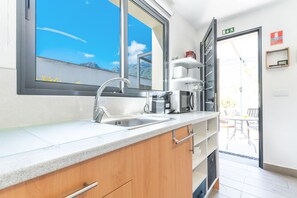 Eine moderne Küche mit einem großen Fenster, einer Spüle, einer Kaffeemaschine und einem Essbereich, der durch die Tür sichtbar ist.