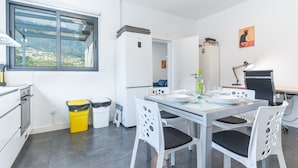 A modern kitchen with a dining area, a view through a large window, and a small trash bin. - Casa Barranca by Atlantic Holiday (São Vicente)