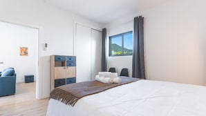 A hotel room with a bed, a desk with drawers, a chair, a window with a view of hills, and a poster on the wall. - Casa Barranca by Atlantic Holiday (São Vicente)