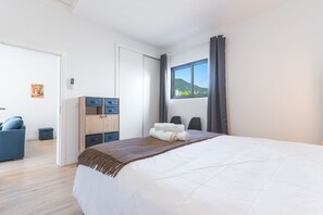 Ein Hotelzimmer mit Bett, Schreibtisch mit Schubladen, Stuhl, Fenster mit Blick auf Hügel und einem Poster an der Wand.