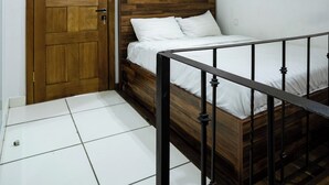 A bedroom with a wooden door, a bed with white bedding, and a tiled floor. - Lobster Beach Resort (Lekki)