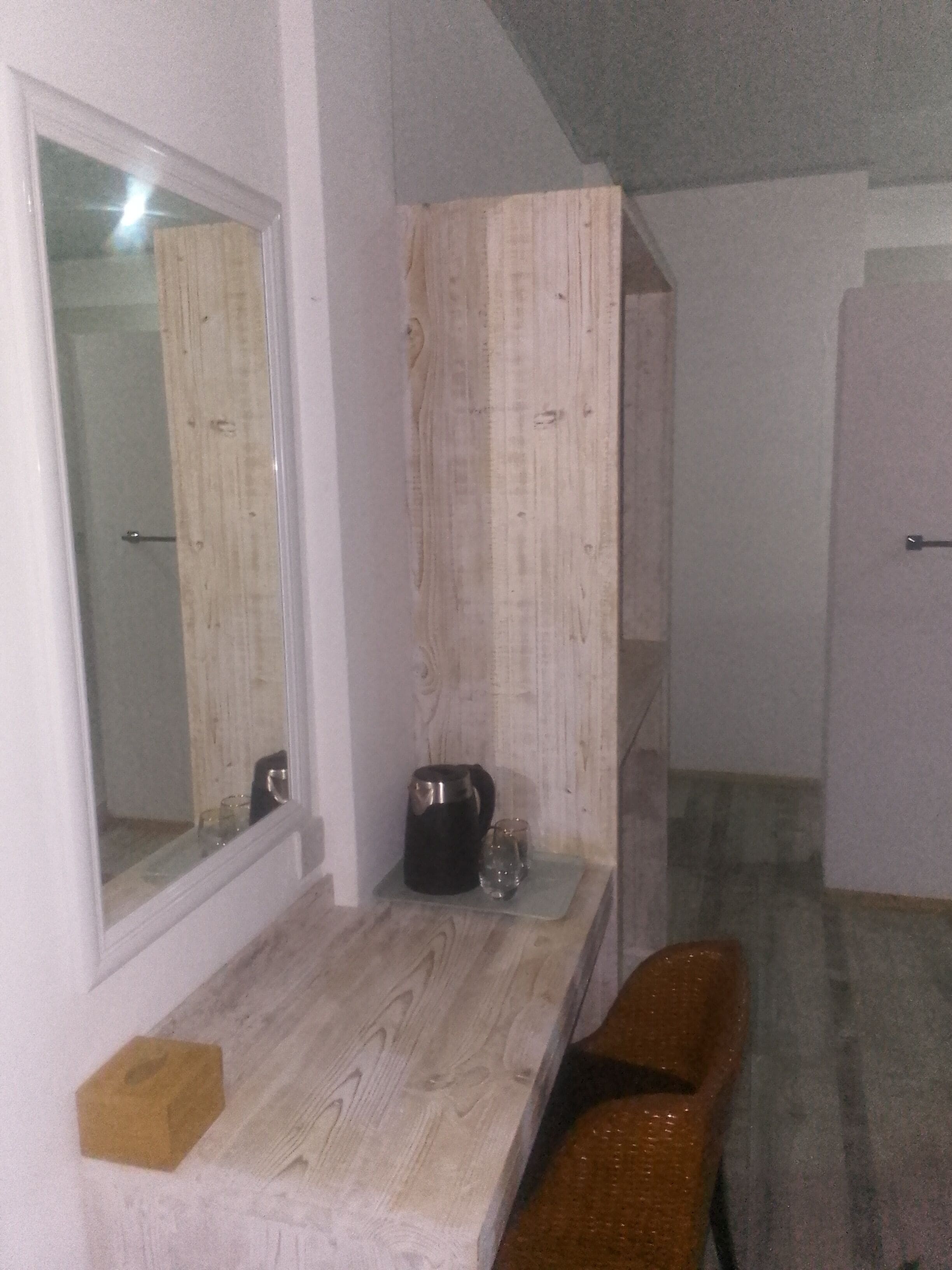 A room with a wooden bench, a small table with a kettle and glasses, and a mirror on the wall.