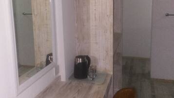 A room with a wooden bench, a small table with a kettle and glasses, and a mirror on the wall.