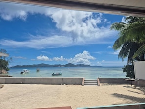 A beach view with boats, a palm tree, and a concrete structure. - Unique beach front hotel (La Digue)