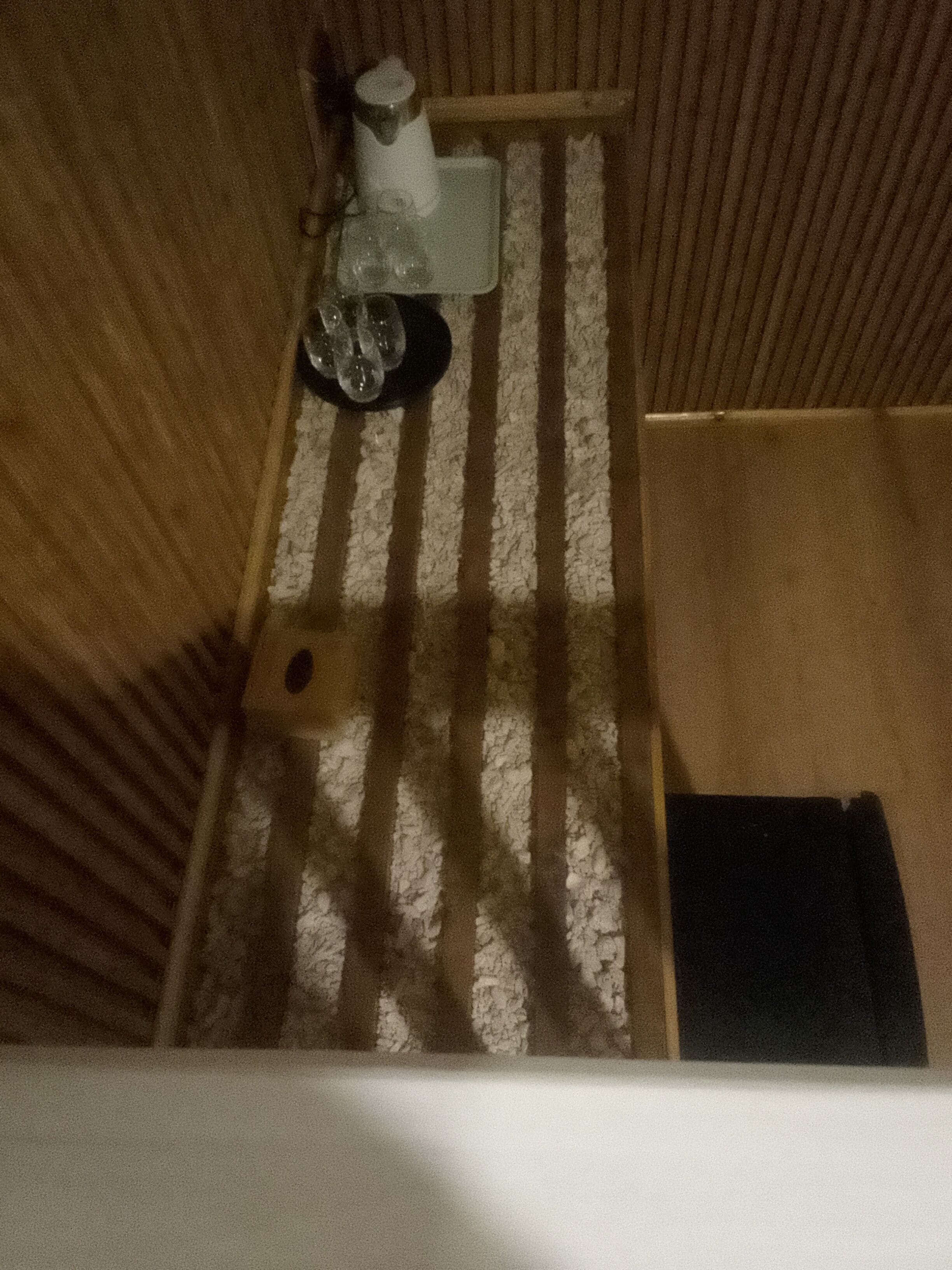 Un interior estrecho y de madera a rayas, con una pequeña mesa y una silla, un objeto blanco sobre la mesa y un objeto negro en el suelo.