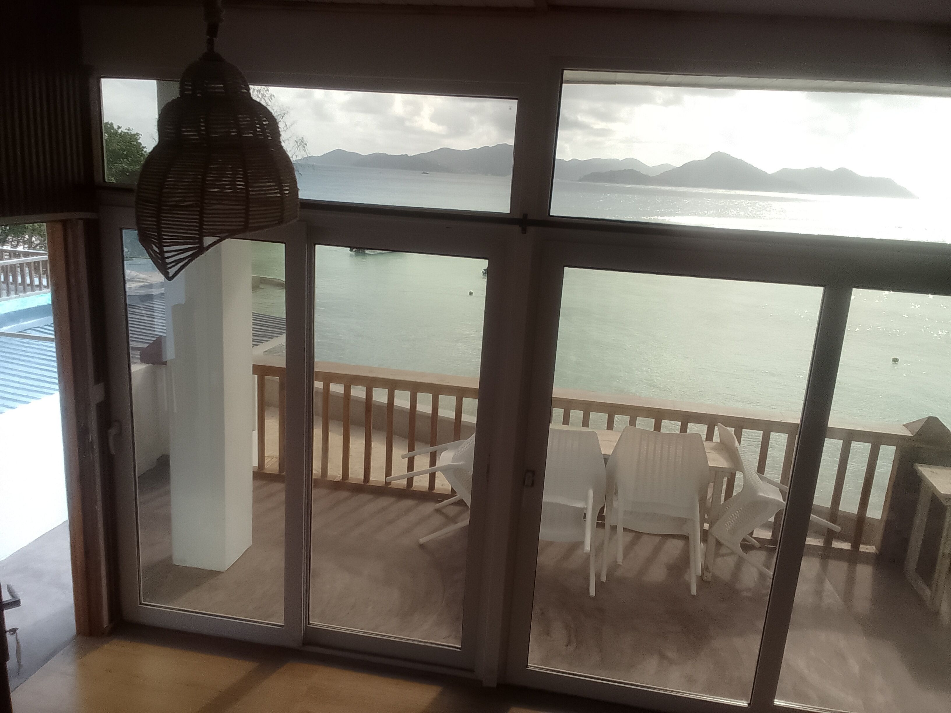 Una habitación con vista al mar, un balcón con sillas y una lámpara colgante.