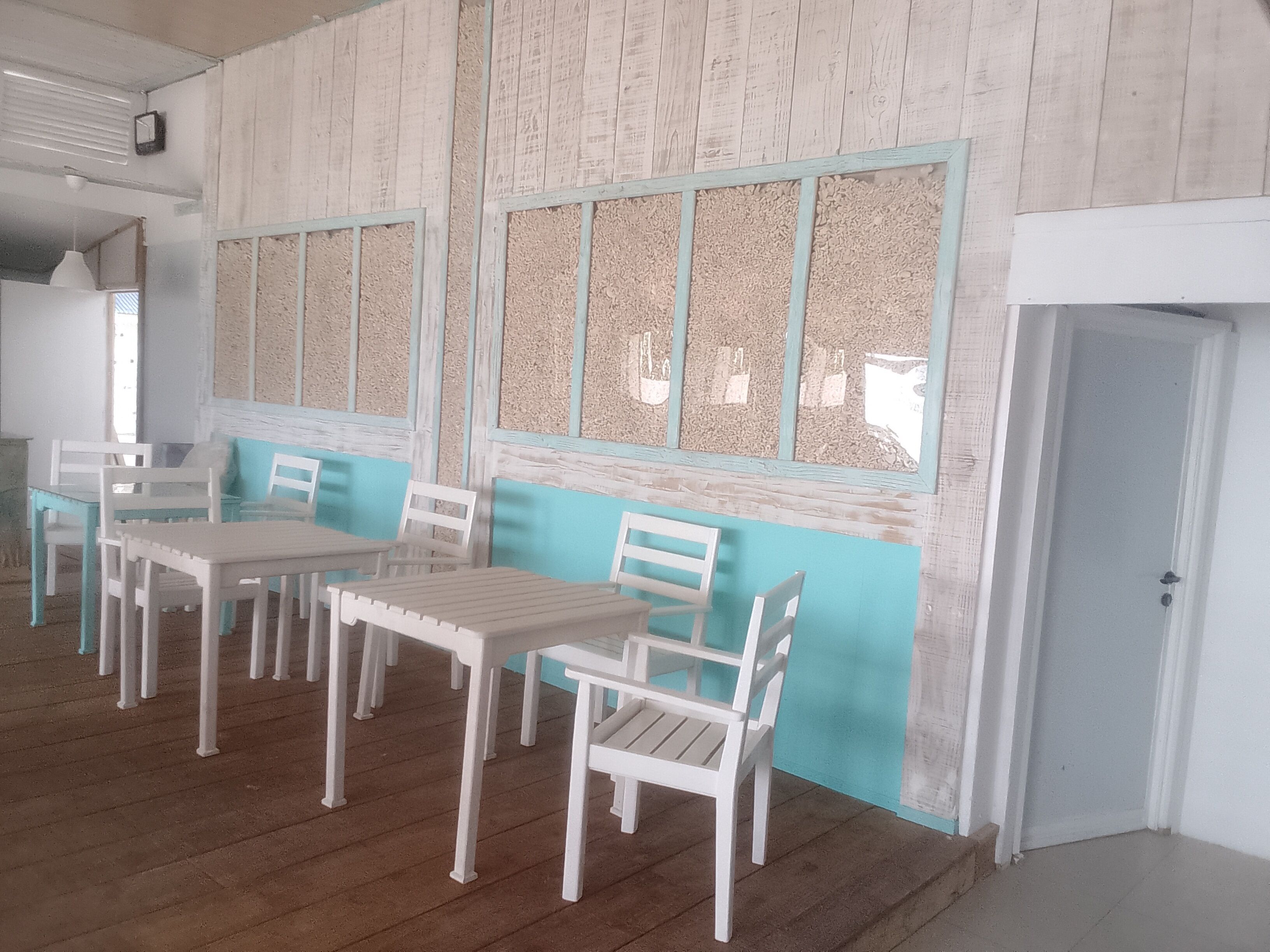 A room with a wooden floor, white tables and chairs, and a door.