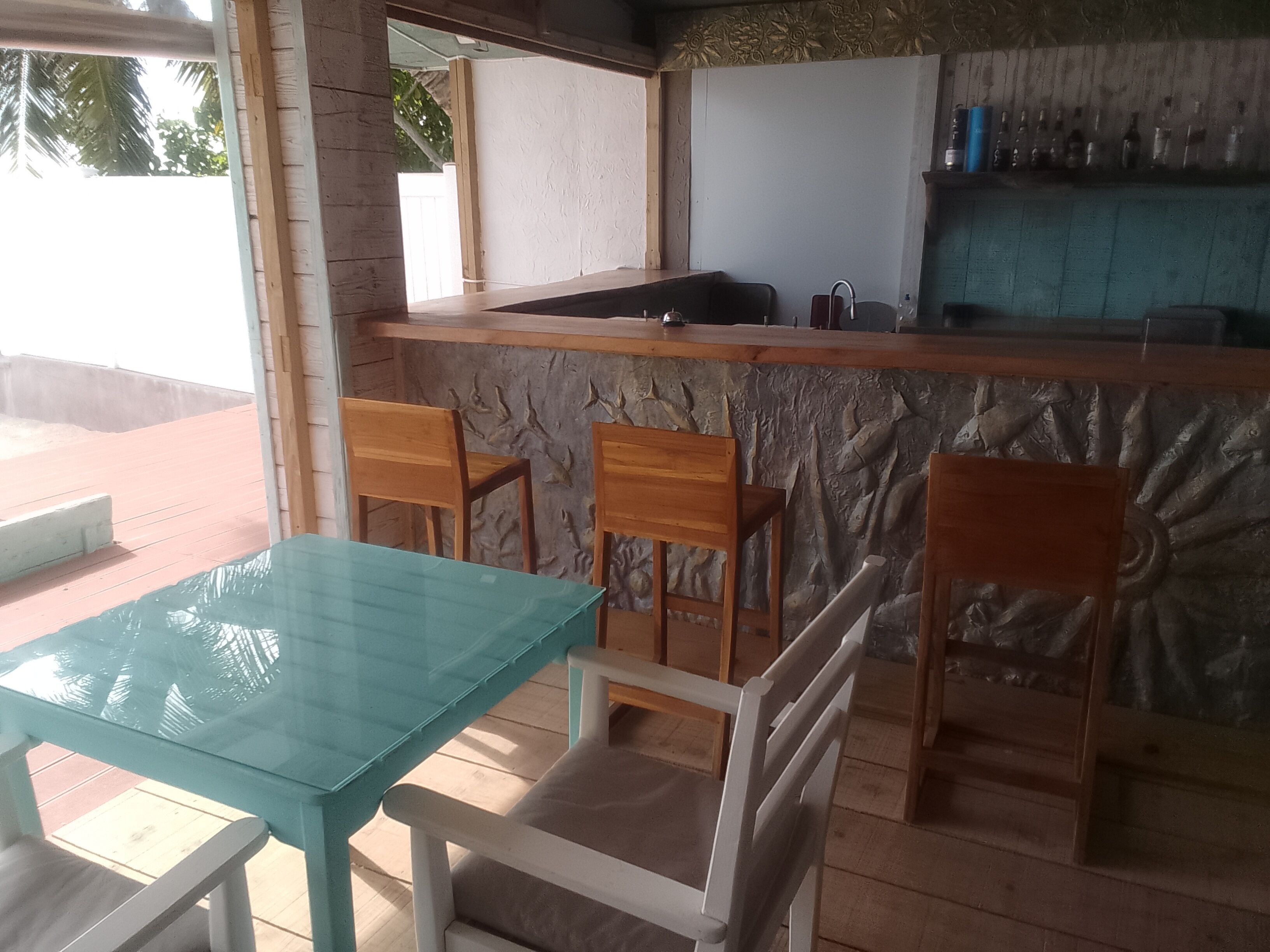 Une cuisine avec un mur recouvert de pierres, des chaises en bois, une table en verre et un coin bar avec des bouteilles.