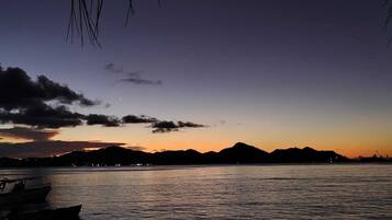 A calm body of water with boats, a mountain range in the background, and a clear sky.
