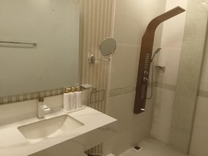 A bathroom with a white sink, a mirror, a shower with a handheld showerhead, and toiletries on the counter. - Unique beach front hotel (La Digue)