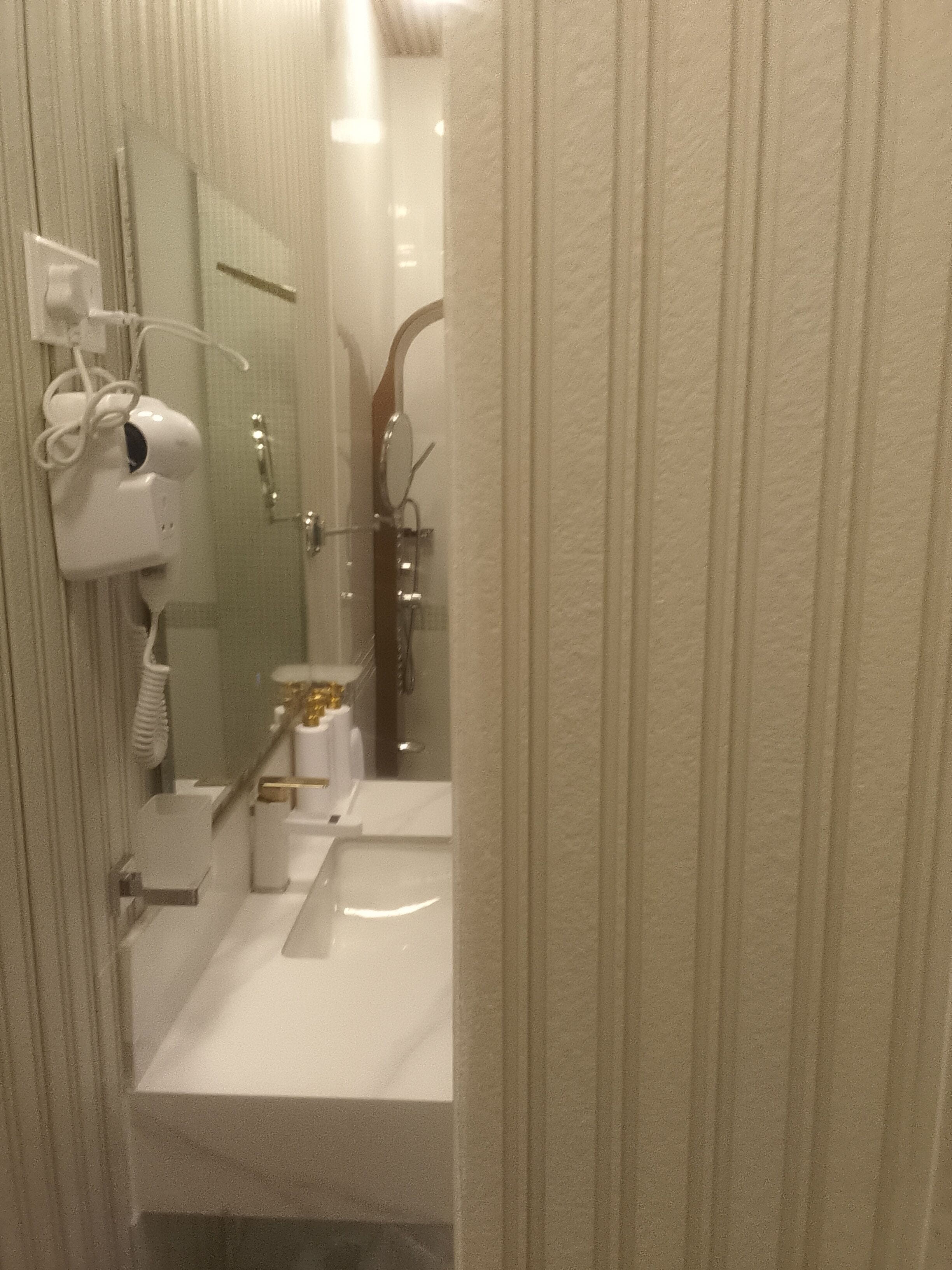 Un baño con lavamanos blanco, un espejo, secador de pelo y zona de ducha.