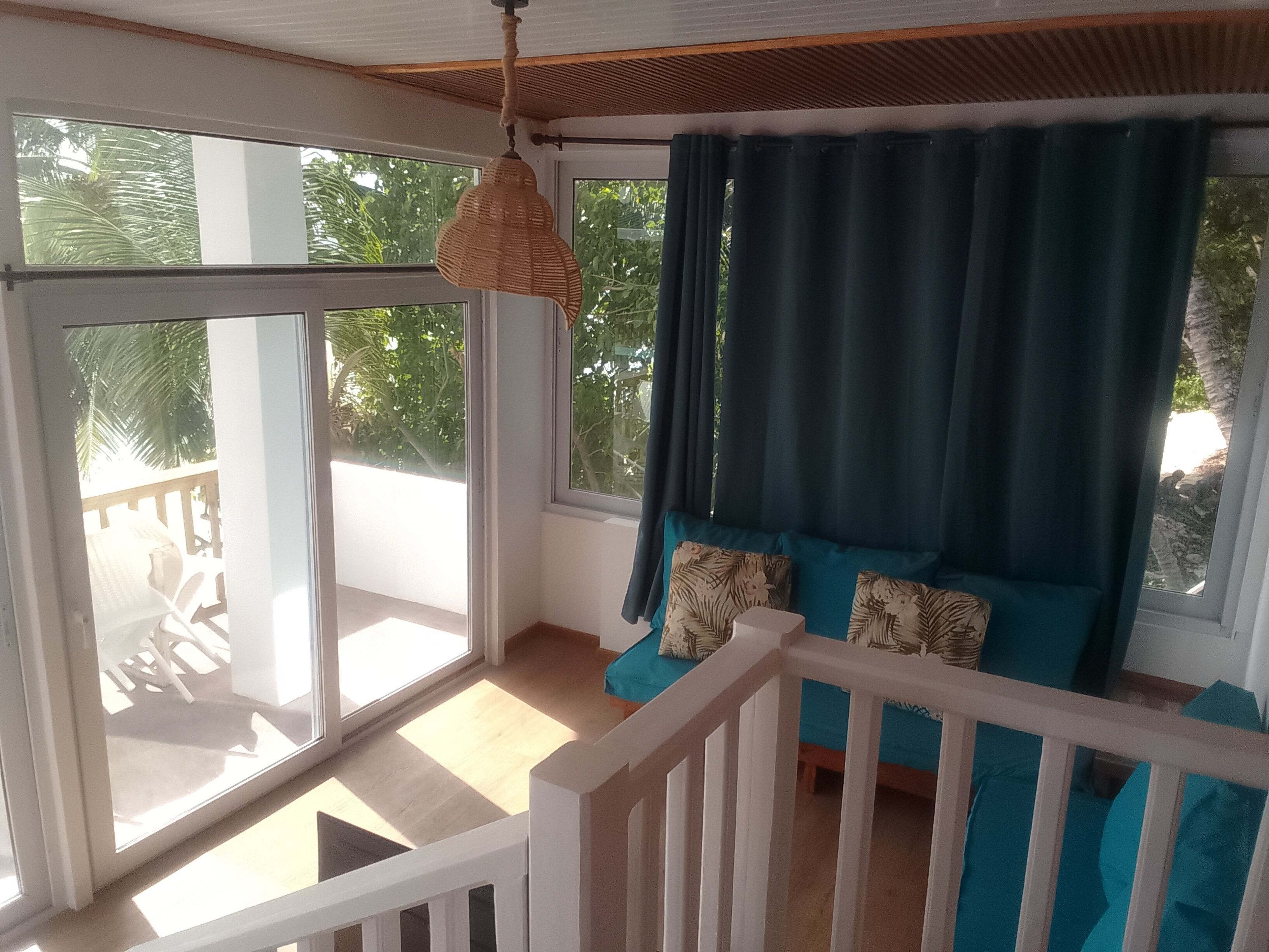 A room with a balcony, a white railing, and a view of greenery outside.