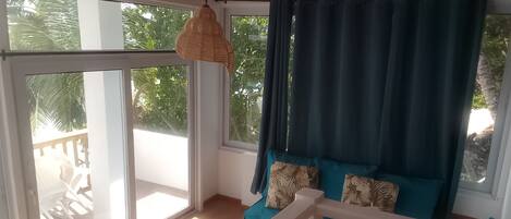 A room with a balcony, a white railing, and a view of greenery outside.