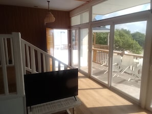 A room with a staircase, a television, and large sliding glass doors leading to an outdoor deck with chairs. - Unique beach front hotel (La Digue)