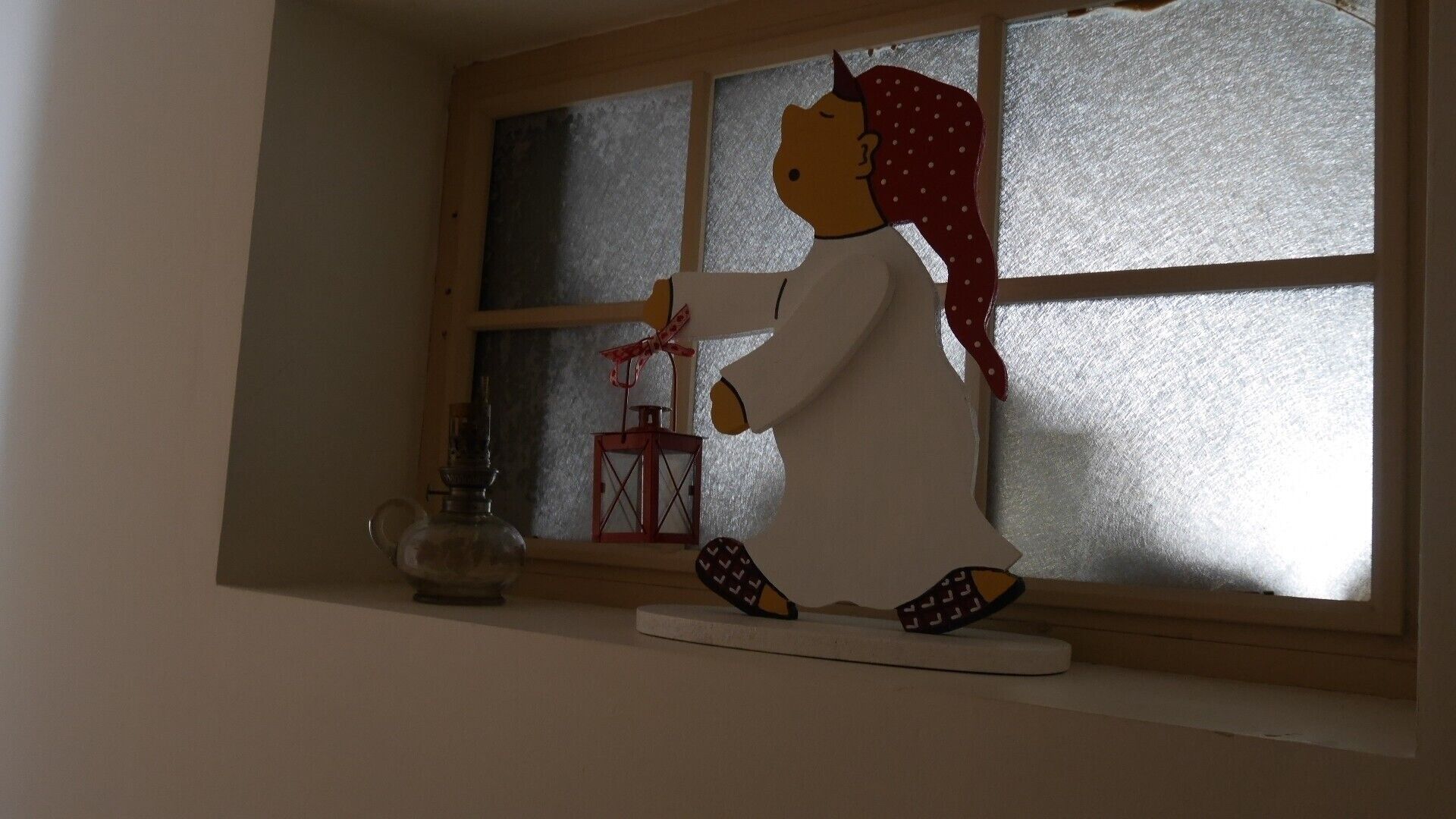 Eine Figur einer Person in traditioneller Kleidung sitzt an einem Fenster mit Laterne und Flasche.