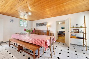 A dining area with a wooden table and bench, a kitchen in the background, and a patterned floor.