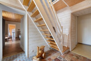 A wooden staircase with a handrail, a patterned floor, and a dining area in the background.