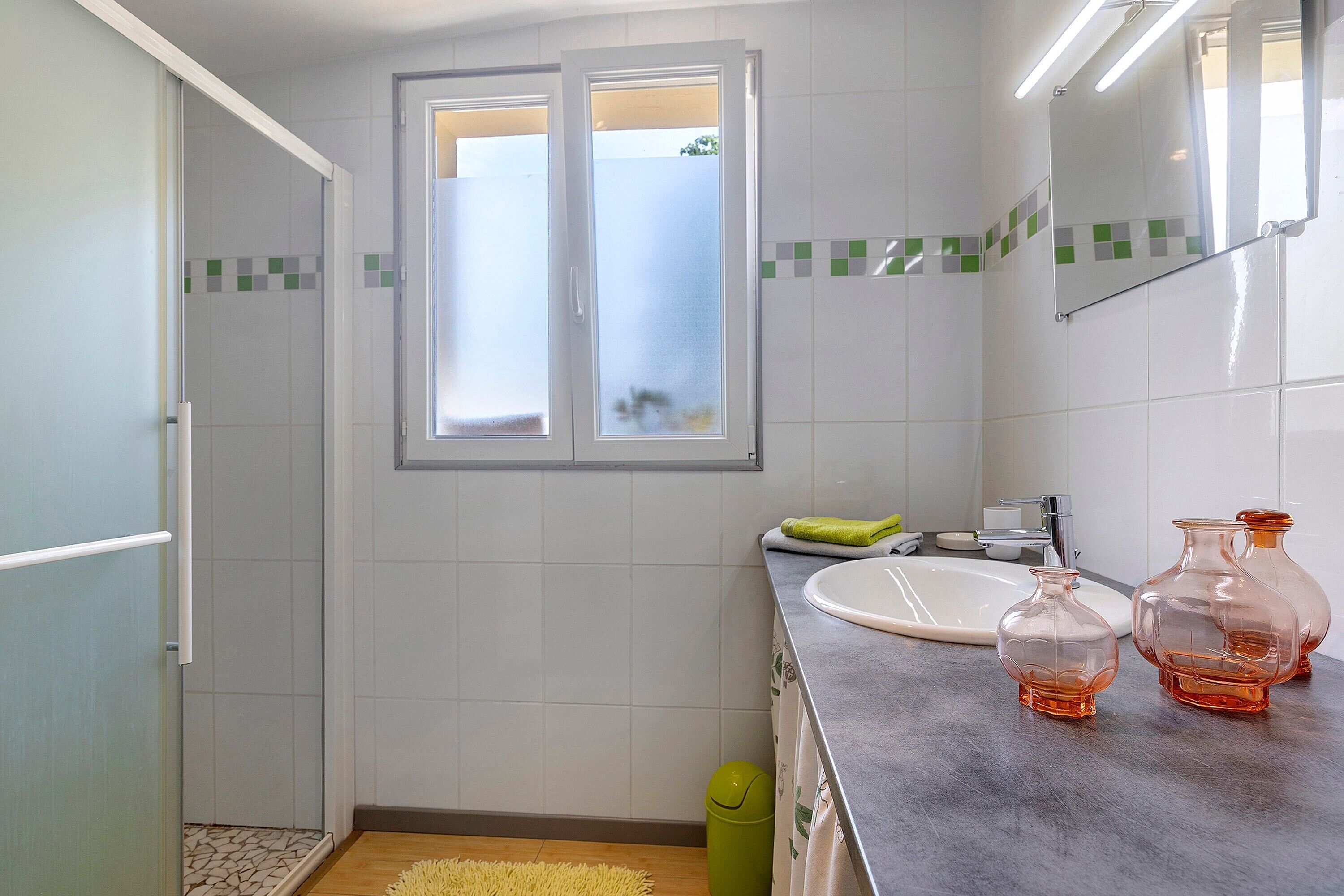 Une salle de bain avec une douche, un lavabo et deux récipients en verre posés sur le comptoir.