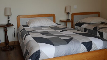 A hotel room with two beds, each with a wooden headboard, a patterned bedspread, bedside tables with lamps, and a wall socket.. Spacious Holiday Home Laplanque – Marais Poitevin in Vendée!