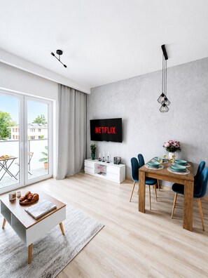A modern living room with a flat-screen TV, dining table, chairs, and a sofa. - Lumina Apart neat ZOO in Lodz Parking (Łódź)