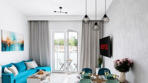 A modern living room with a sofa, coffee table, dining table with chairs, and a TV mounted on the wall. - Lumina Apart neat ZOO in Lodz Parking (Łódź)