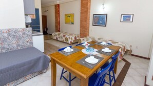 A dining area with a wooden table set for four, blue chairs, and a sofa in the background. - Direita S.Antonio-Comfort Street Quarto e sala para 5 pessoas, vista c.historico. (Salvador)