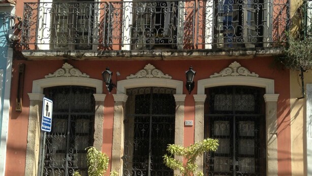 A building with ornate iron gates, a balcony with a wrought iron railing, and two potted plants in front. - Direita S.Antonio-Comfort Street Quarto e sala para 5 pessoas, vista c.historico. (Salvador)
