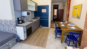 A compact kitchen with a microwave, coffee maker, and a dining area with blue chairs and a wooden table. - Direita S.Antonio-Comfort Street Quarto e sala para 5 pessoas, vista c.historico. (Salvador)