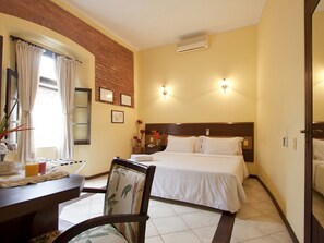 Een hotelkamer met een bed, nachtkastje, stoel en een raam met gordijnen.