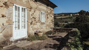 Ein rustikales Steinhaus mit zwei Fenstern in weißem Rahmen, einem kleinen Tisch im Freien und einer Topfpflanze.