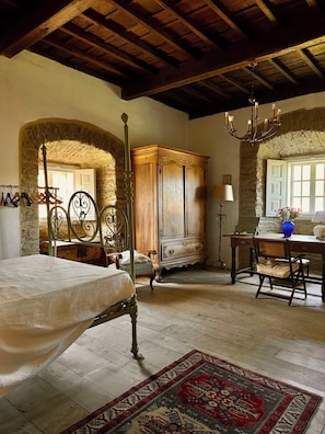 A bedroom with a four-poster bed, a wooden wardrobe, a desk with a chair, and a chandelier.