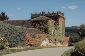 A historic stone building with ivy-covered walls and a tower, surrounded by a rural landscape.