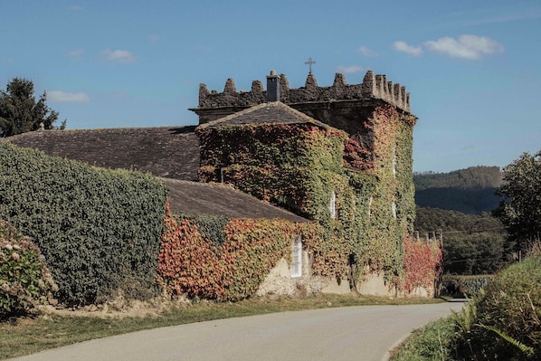 A historic stone building with ivy-covered walls and a tower, surrounded by a rural landscape.