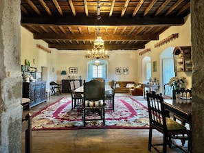 A spacious room with a wooden ceiling, a chandelier, a dining table with chairs, a sofa, and a patterned rug.