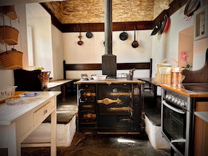 A rustic kitchen with a wood-burning stove, hanging pots, and a vintage oven.