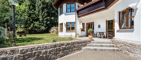 Una casa de dos pisos con un muro de piedra, escalones de madera y un jardín.